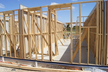 A mostly-bare wooden house frame occupied with a few scattered drywall sheets